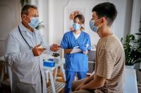 teenage boy sitting on exam table in front of physician